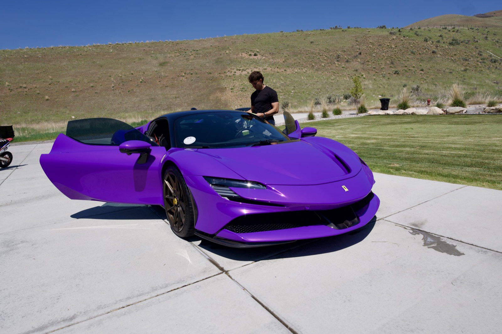 Purple Ferrari parked on concrete with green hills behind