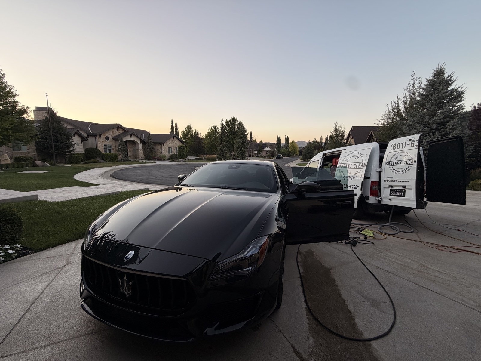 Black Maserati being detailed in a driveway next to the Squeaky Clean van at dusk